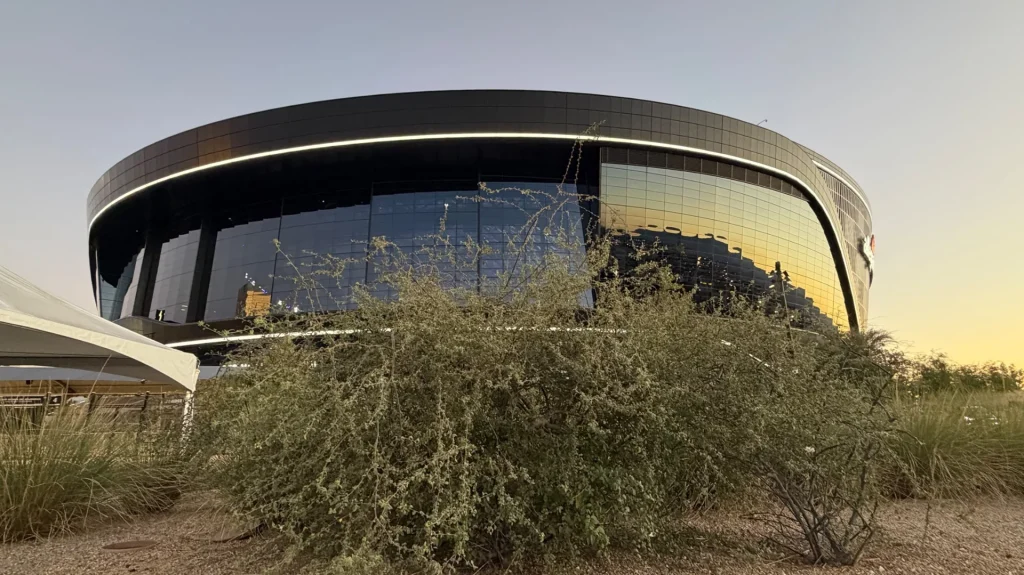 Curved dark exterior and reflective glass façade of Allegiant Stadium at sunset.