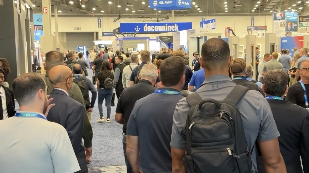 Attendees walking among exhibitor booths on the GlassBuild America show floor.