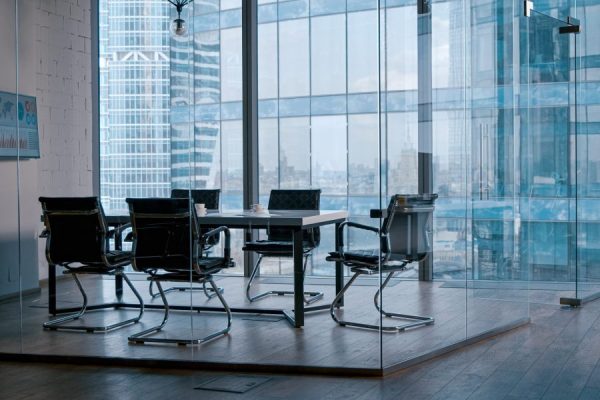 Modern commercial conference room enclosed by clear glass walls overlooking city buildings