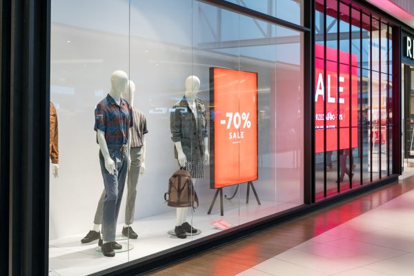 Modern glass retail storefront with mannequins, merchandise displays, and illuminated sale signage
